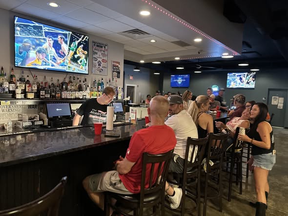Customers at the bar watching the game on big TVs with beers