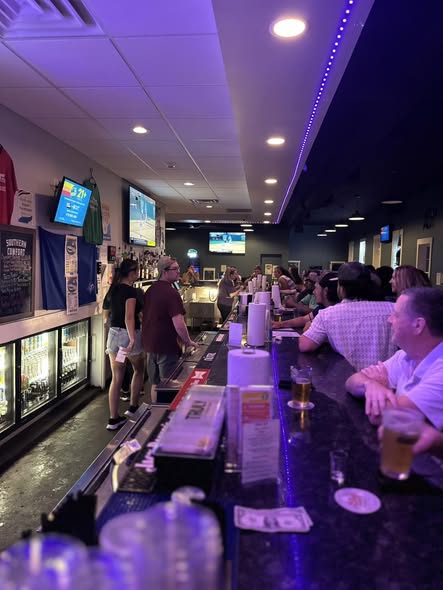 Long bar shot at night with purple LED lighting and customers along the full bar