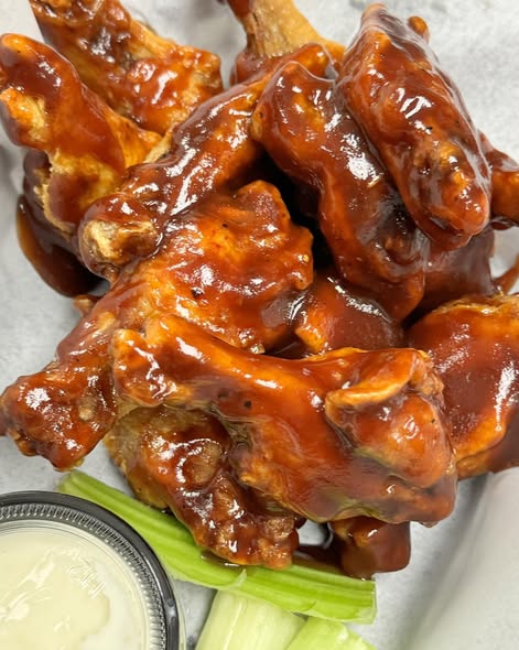 BBQ-glazed bone-in wings glistening with sauce, served in a basket with celery sticks and ranch dressing